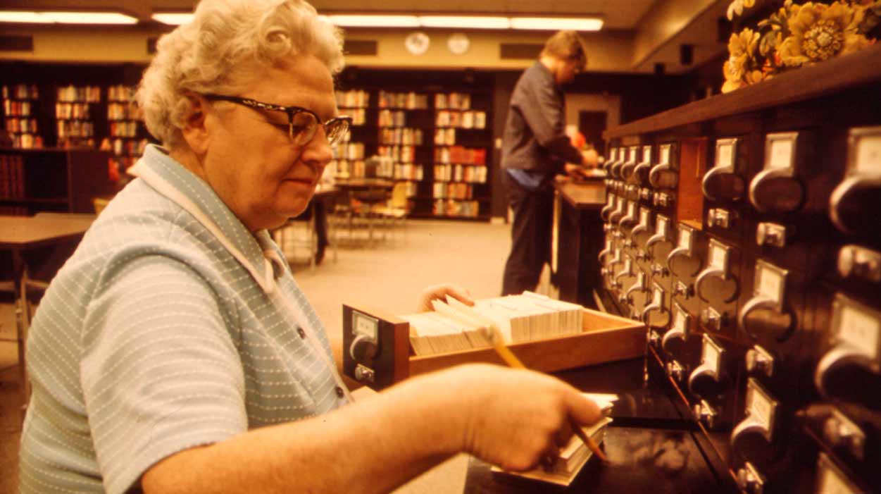Elderly librarian organizes a card catalog
